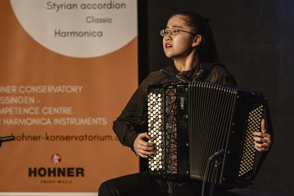 Akkordeonspielerin auf der Bühne im Hintergrund das Plakat von Akkordeon grenzenlos in orange